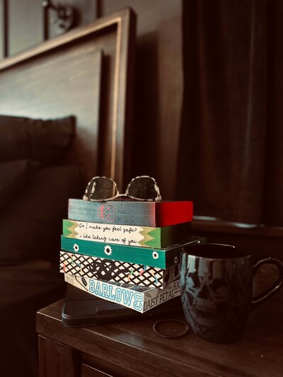 Nightstand with handmade sprayed-edge books from Sprayed Your Pages, reading glasses, and a coffee mug, styled to showcase cozy reading and collectible book aesthetics.