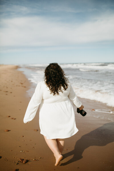 Valerie Doucette, Ottawa Gatineau branding photographer, walking at the shore of the beach with her camera out