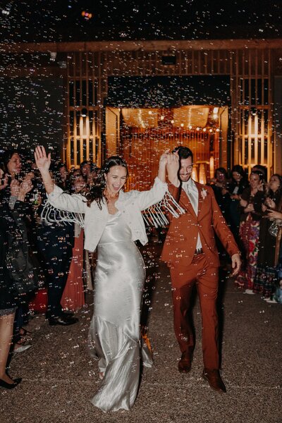 Bride and groom exit reception excitedly  through bubbles