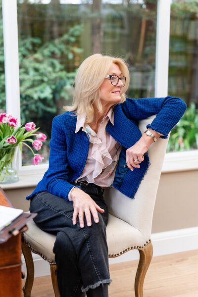woman in blue blazer sitting on a chair with pen in her hand