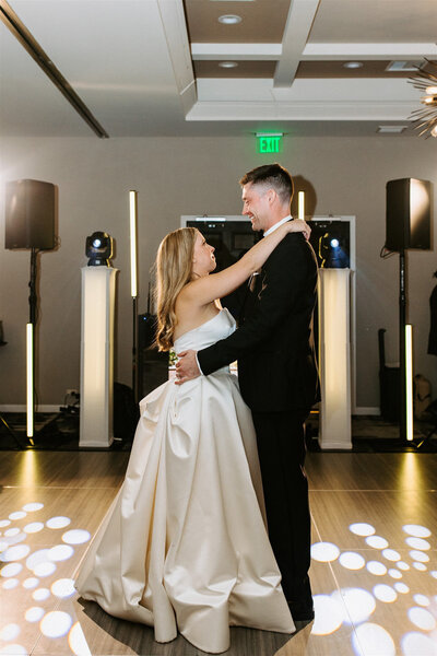 Bride and groom sharing their first dance under elegant spotlight lighting on the wedding reception dance floor.
