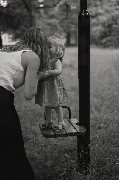 Liten tjej sträcker sig fram och pussar sin mamma i en park.