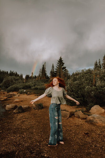 senior girl dancing in rain under rainbow