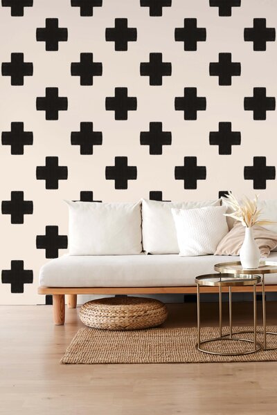 Soft clay colored wallpaper with symmetrical tiles in the form of hand drawn black Swiss crosses adorn the walls of a living room with a white couch and boho decor. Style bohemian, modern, vintage modern, whimsigoth,