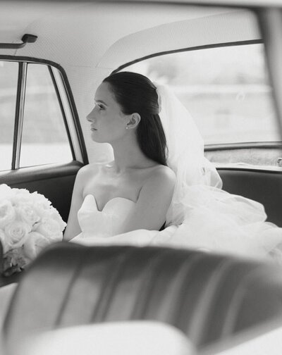 Black and white image of a bride looking out a car window