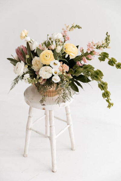 Large centerpiece of flowers in vase set on a white stool