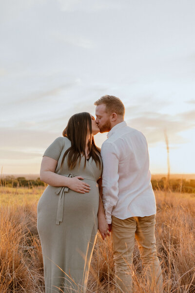 Couple kissing at sunset, mother is pregnant and holding her belly