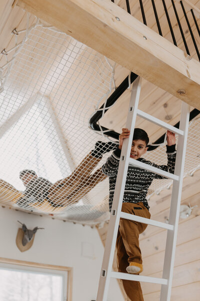 Two kids going up to relax at an indoor net hammock bed at Chalets Prunella No. 1, Quebec.