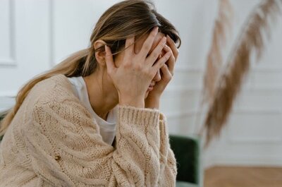 woman sitting in with her hands over her face because she doesn't feel good