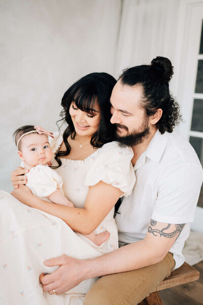 five month old baby girl with a pink bow sitting on her mom's lap looking up at the photographer