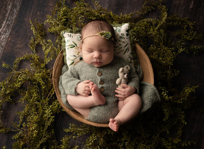 sleeping baby laying in a brown bowl wearing a green knit romper