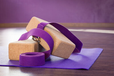 A purple yoga mat with a purple strap and cork yoga props
