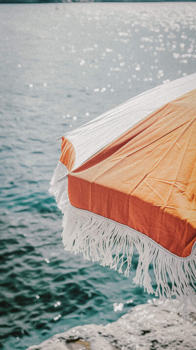 Orange and white beach umbrella with turquoise water behind