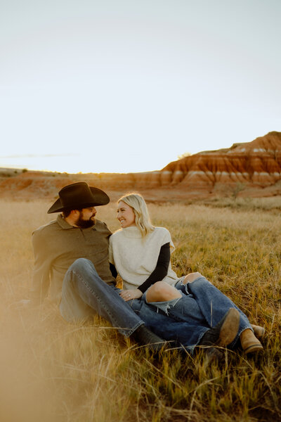 future ranch wedding couple sitting in a field together for engagement
