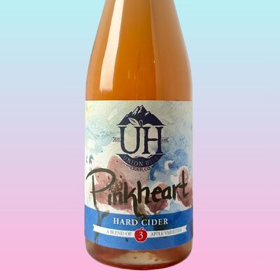 A bottle of Pinkheart hard cider made by Union Hill Cider Co on a pink background.