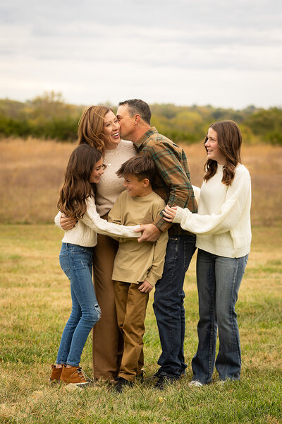 family smiling and embracing while standing in a field