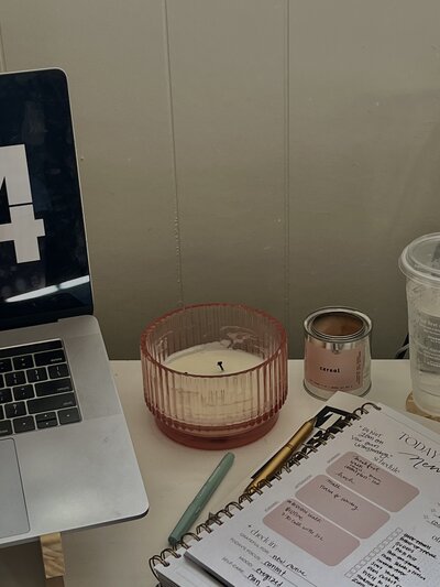 Desk scene of a laptop, notebook, pens, and candle