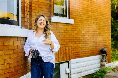 Woman holding camera laughing while in front of brick building