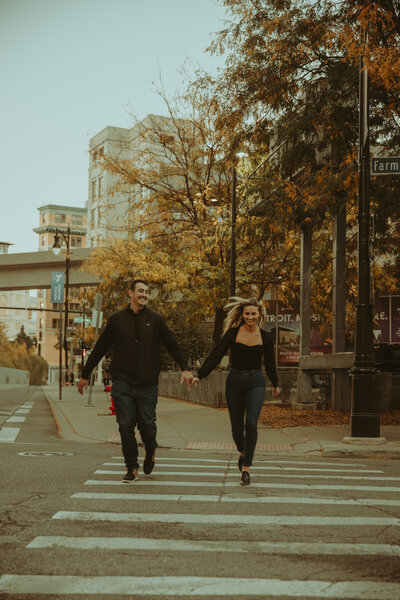 Engaged couple holds hands and laughs and run down the crosswalk