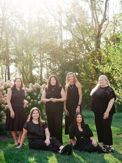We Do Events wedding planning team of 5 women in black outfits standing in front of a white wall