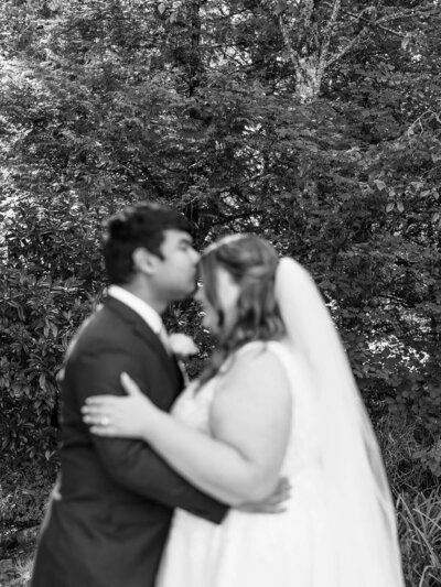 Out of focus shot of a groom kissing the bride's forehead, representing the photo style of wedding photographer Among The Oaks.