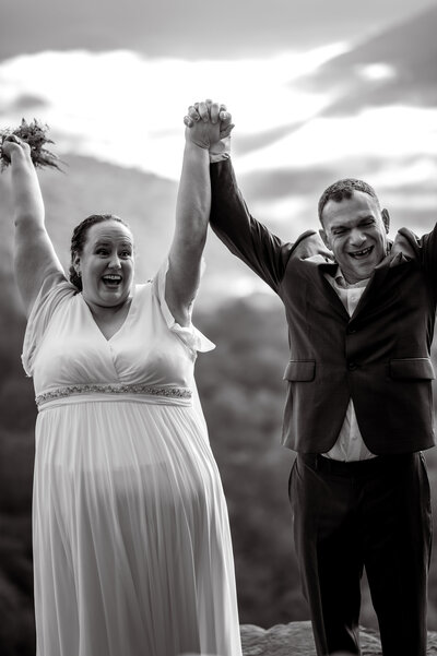 Couple cheers by holding hands in the air as they shout for joy after they elope in the catskills.
