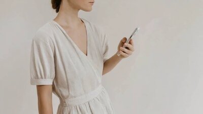 Kvinna i ljus klänning håller mobiltelefon – reflektion och fördjupning kring medberoende.