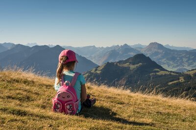 Young girl with a pink backpack and hat sitting at the summit of a mountain after a hike