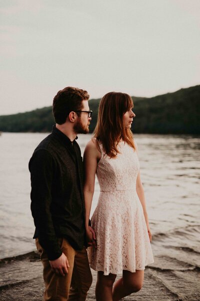 Engaged couple holds hands and looks off into the sunset