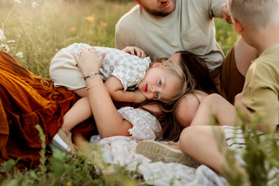 Little boy lays on mom while looking at Kansas City portrait photographer in field for family session.