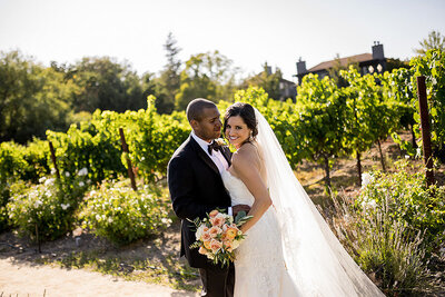Romantic newlywed couple portrait with bride in flowing veil and groom in black suit among Estate Yountville gardens, professional Bay Area wedding photographer