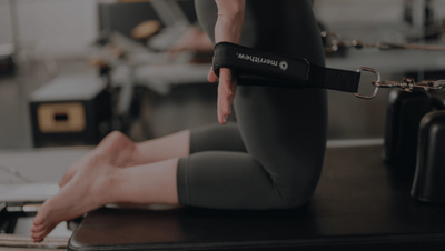 woman kneeling on a pilates reformer with hands in resistance bands 