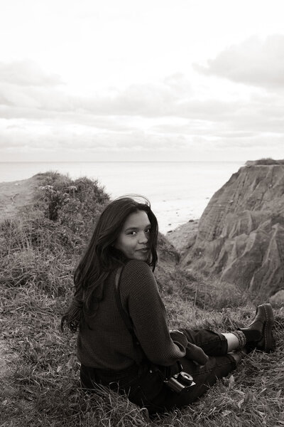 woman sitting on cliff holding out camera