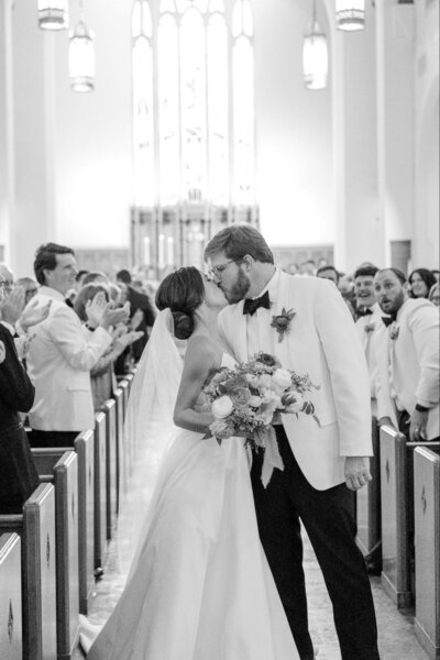 Black and white photo of bride and groom kissing in the aisle