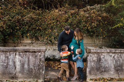 A family of four enjoying a moment together outdoors during a family photography package session, with a parent each holding hands with one child.