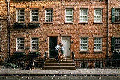 A couple kiss while taking engagement photos in the West Village with their dog nearby.