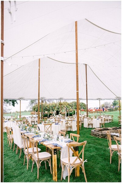 interior of sailcloth tent filled with farm tables, crass-backed chairs and string lights