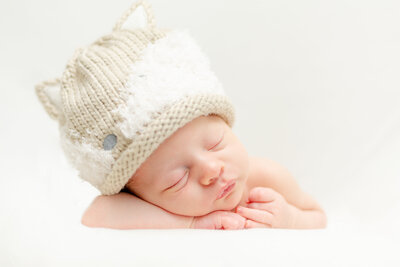 Portrait of a newborn wearing a fox hat sleeping with head in hands