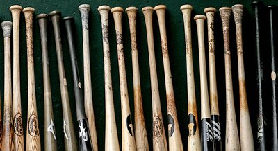 Baseball bats lined up against a green wall in the dugout.