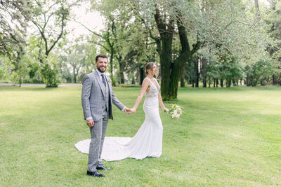This stunning photograph captures the bride and groom holding hands during their portrait session at the Norland Historic Estate in Lethbridge. The groom looks confidently toward the camera, while the elegant estate setting enhances the timeless beauty of this moment.