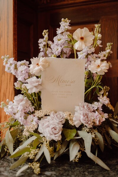 Mimosa bar sign tucked in a flower bouquet