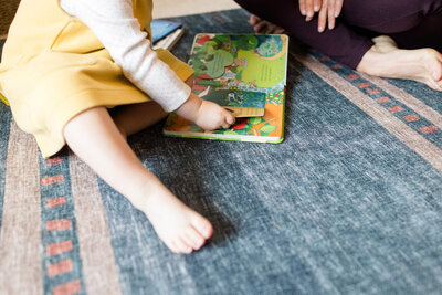 Toddler playing with a book while they sit next to their mom