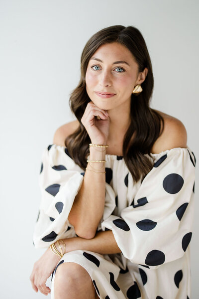 Natasha Churches, owner of Aisle & Co., poses for a headshot in all white while holding champagne.