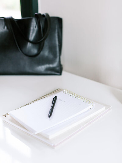 Stack of notebooks laying on a white table next to a black leather bag