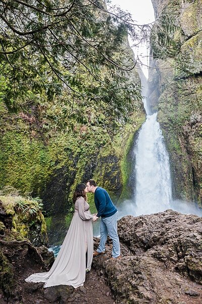 Portland pregnant mom in front of waterfall near portland oregon kissing partner