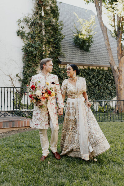 A couple walks with an Anthousai bouquet, dressed in traditional Indian wedding garments at the Oklahoma City Golf and Country Club