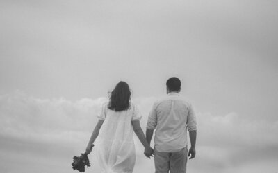 Black-and-white photo of a couple holding hands, capturing a timeless and intimate moment of love and connection with classic, artistic charm