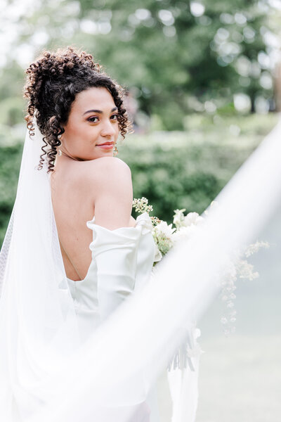 bride holding a bouquet and posing as veil flies in the wind