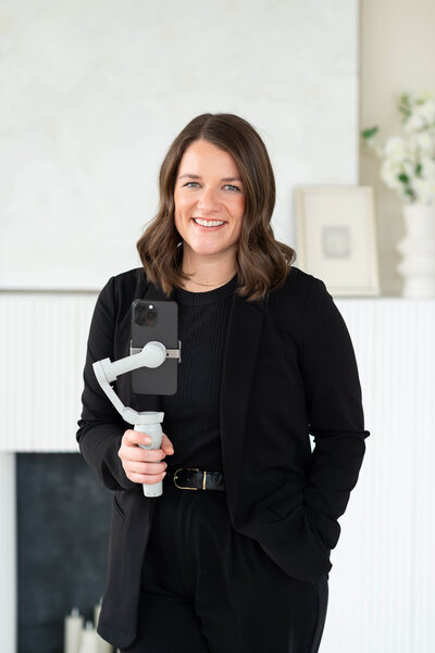 a photo of an Ottawa content creator in a black pantsuit holding her camera and smiling