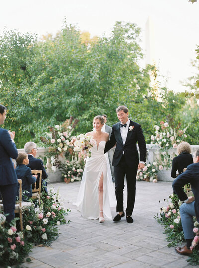 Bride and groom walking back up the aisle at DAR Constitution Hall in Washington DC, surrounded by romantic blush and ivory floral aisle arrangements. Luxury wedding ceremony flowers by Springvale Floral, editorial florist serving DC, Virginia, and Maryland.
